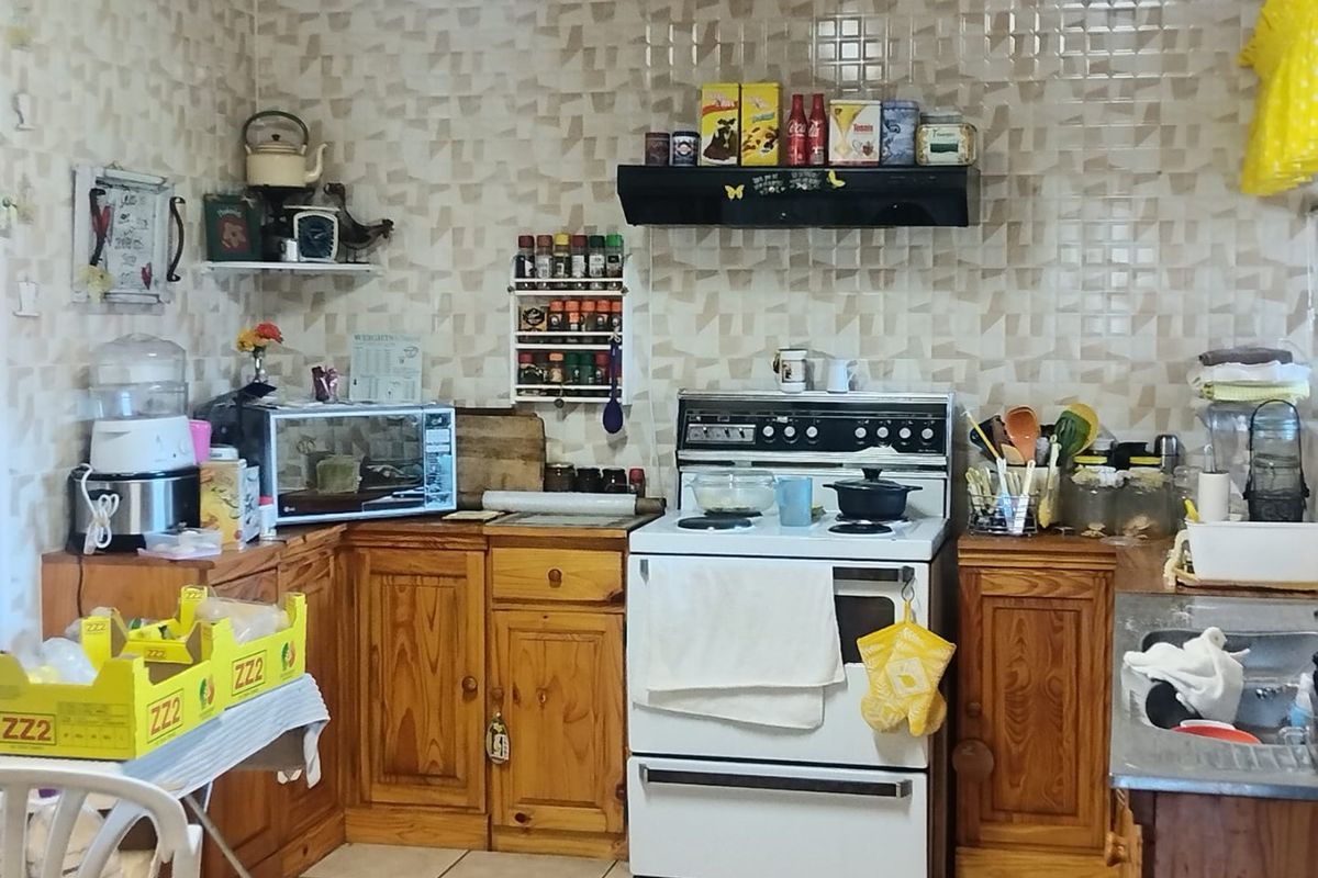 A functional kitchen featuring wooden cabinetry, a freestanding stove with extractor fan, and tiled splashbacks, offering potential for modernization.