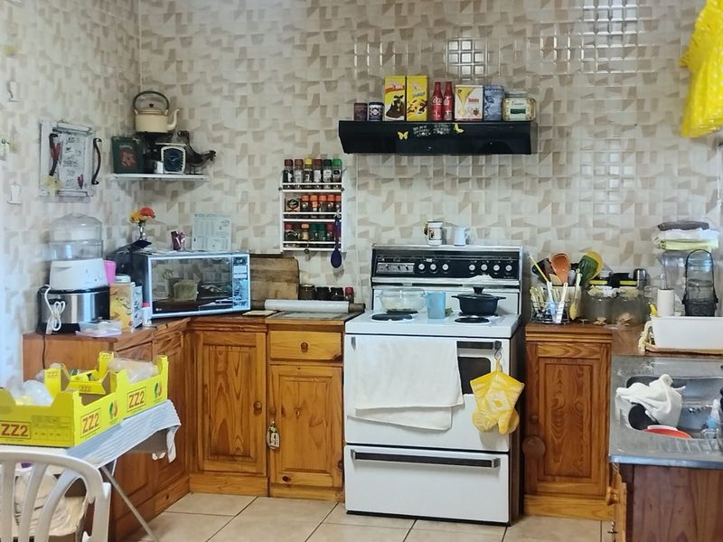 A functional kitchen featuring wooden cabinetry, a freestanding stove with extractor fan, and tiled splashbacks, offering potential for modernization.