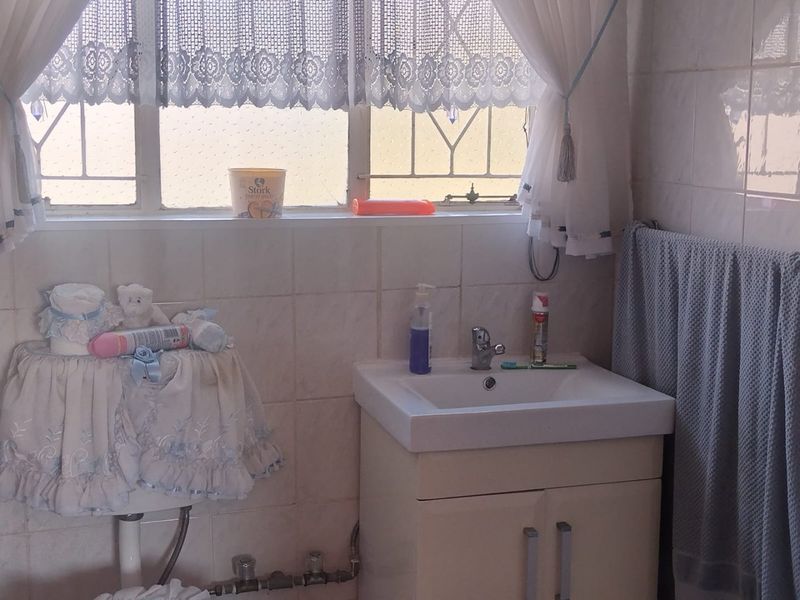 A functional bathroom featuring a vanity cabinet with a ceramic basin, chrome mixer tap, and tiled walls with security burglar bars on the window.