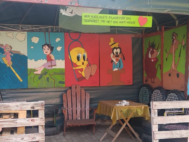 A covered outdoor patio area featuring decorative wall murals and paved flooring, suitable for casual outdoor seating and entertainment.