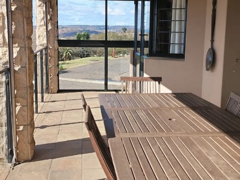 Covered patio featuring stone pillar accents, tiled flooring, and glass balustrades, offering an outdoor entertainment space with scenic views.