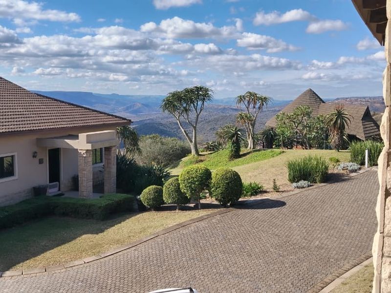 Elevated view overlooking a well-maintained townhouse property with a paved driveway, stone-clad exterior features, and scenic mountain landscape in the background.