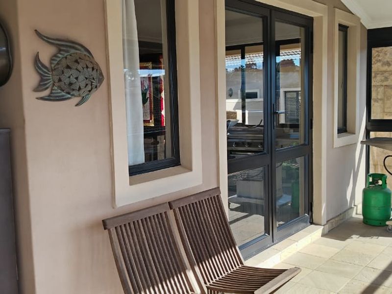 A covered patio area featuring tiled flooring and aluminium-framed glass doors, providing a functional outdoor space for relaxation and entertaining.