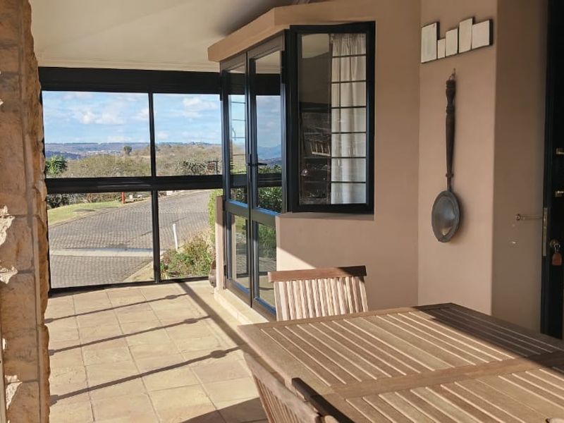A covered patio area featuring tiled flooring, stone cladding accents, and aluminium-framed windows and doors, offering an open-air feel with scenic views.
