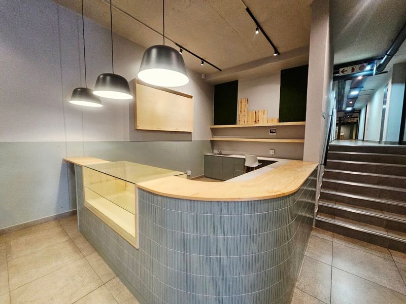 A modern, well-lit reception or utility area featuring a curved tiled counter, built-in cabinetry, and sleek pendant lighting, adjacent to a staircase.