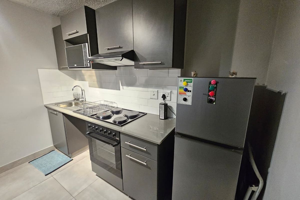 Modern kitchen featuring dark grey cabinetry, stone countertops, subway tile backsplash, and integrated appliances including an oven, hob, and extractor fan.