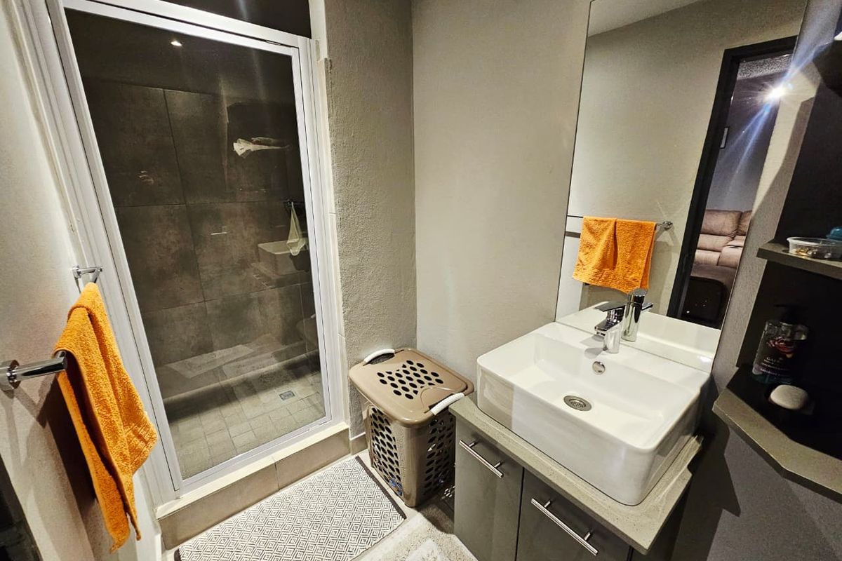A modern bathroom featuring a glass-enclosed shower with dark tiling, a vanity cabinet with a vessel sink, and a large wall-mounted mirror.