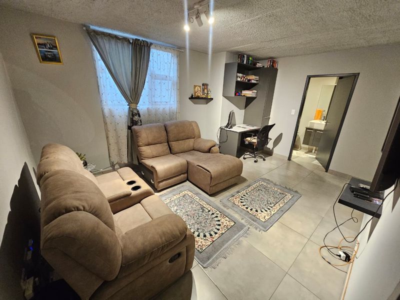 A living room featuring tiled flooring, a built-in shelving unit, and track lighting, with an adjacent bathroom visible through the doorway.