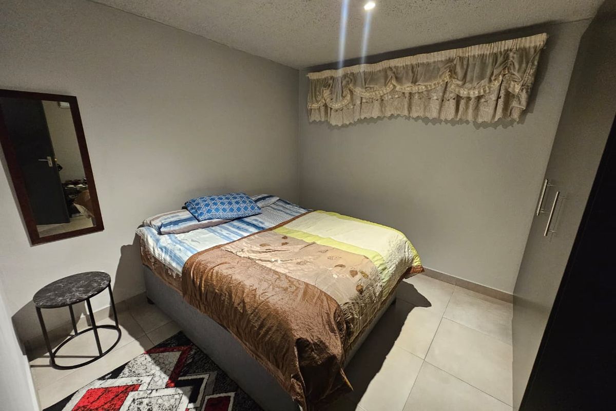 A functional bedroom featuring neutral wall tones, tiled flooring, and a built-in wardrobe, providing a clean and practical living space.