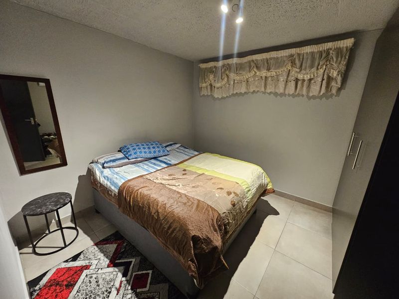 A functional bedroom featuring neutral wall tones, tiled flooring, and a built-in wardrobe, providing a clean and practical living space.