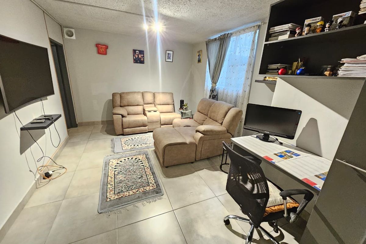A functional living room featuring large format floor tiles, a built-in shelving unit, and a wall-mounted television setup.