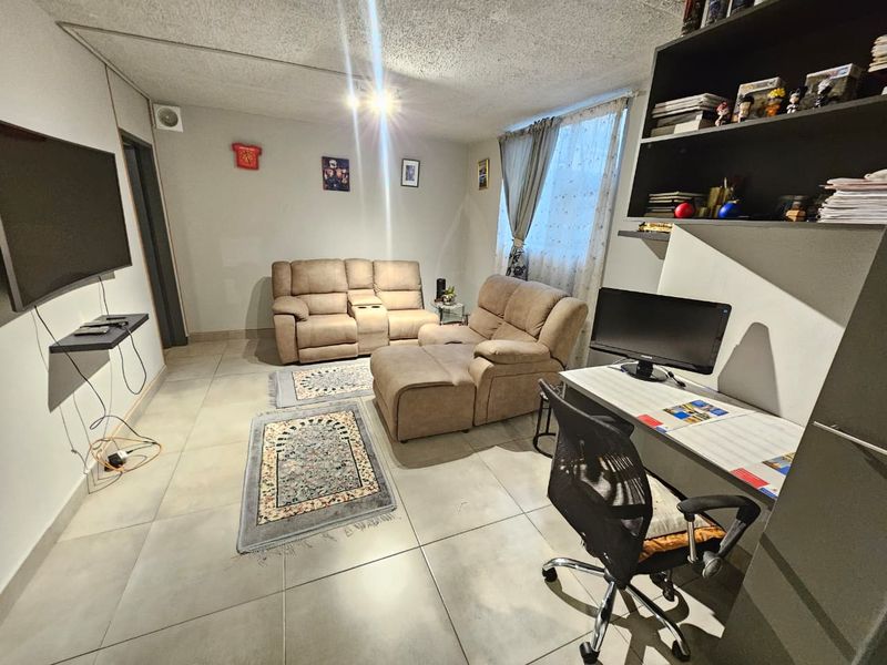 A functional living room featuring large format floor tiles, a built-in shelving unit, and a wall-mounted television setup.