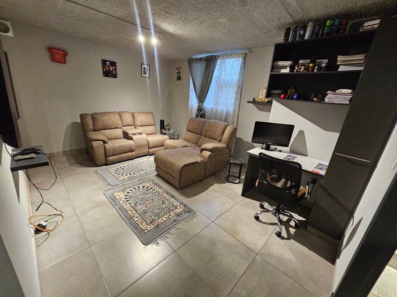 A functional living room featuring large format floor tiles, a textured ceiling, and a built-in wall shelving unit for storage.