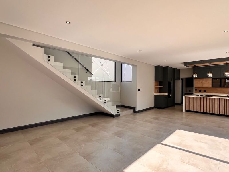 Modern open-plan living area featuring a sleek glass staircase and a contemporary kitchen with a central island and high-end cabinetry.