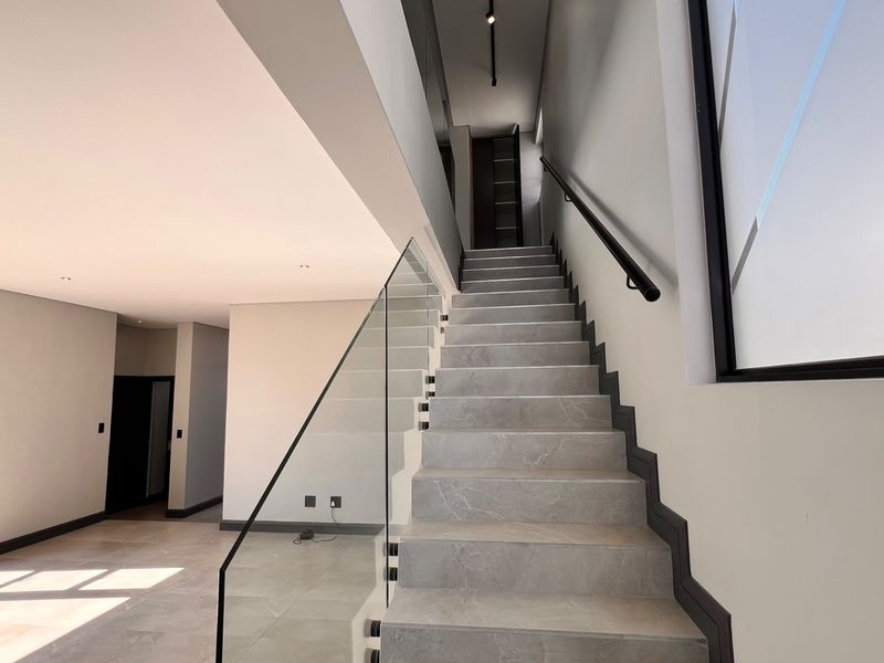 Modern, bright hallway featuring a sleek staircase with glass balustrade, tiled steps, and minimalist architectural design.