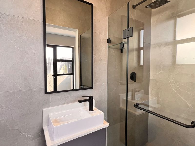 Modern bathroom featuring a vessel sink with black fixtures, a glass-enclosed shower with a rain shower head, and contemporary grey wall tiling.