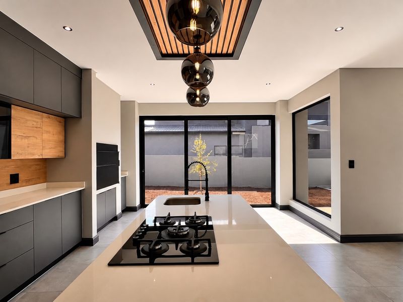 Modern, high-end kitchen featuring a central island with gas hob, sleek cabinetry, stone countertops, and a unique timber slat ceiling detail with pendant lighting.