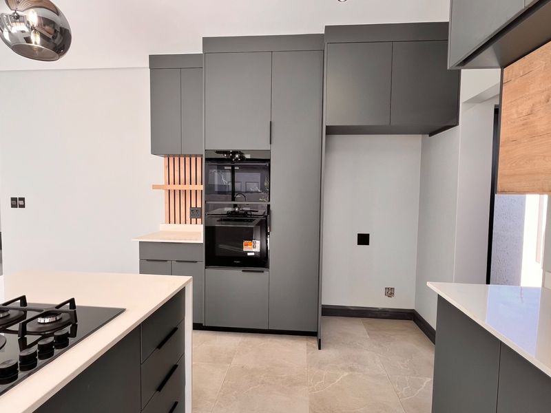 Modern kitchen featuring dark grey cabinetry, stone countertops, integrated oven and microwave, gas hob on the island, and adjacent staircase.