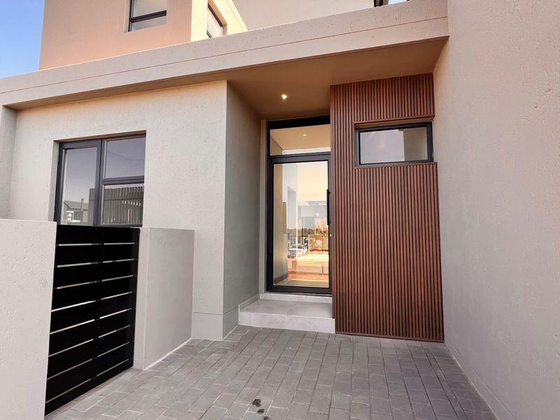 Modern front entrance featuring a sleek glass door, timber slat feature wall, and clean paved entryway.