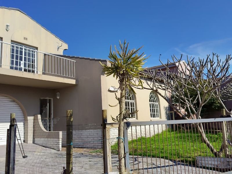 Front elevation of a two-story house featuring a paved driveway, integrated garage, and an upper-level balcony with metal railings.