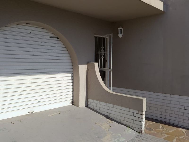 Exterior view of a garage featuring a white roller shutter door, security gate, and brick facade detailing.