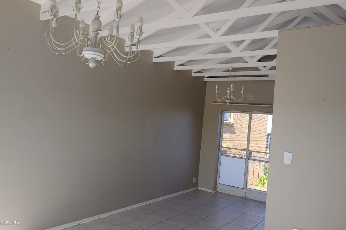 Spacious living area featuring exposed white ceiling beams, tiled flooring, and a sliding glass door providing natural light.