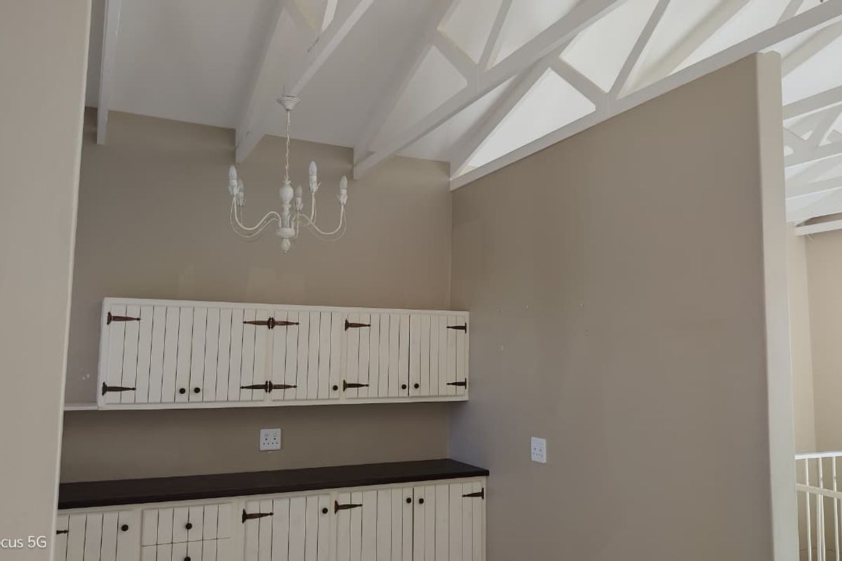 A bright kitchen area featuring white built-in cabinetry, dark countertops, and exposed white roof trusses, offering a clean and functional space.