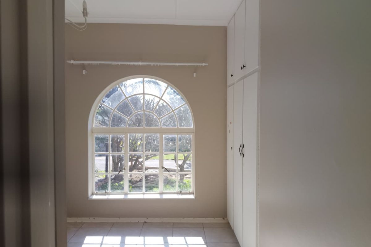 A bright, empty bedroom featuring a distinctive arched window, tiled flooring, and ample built-in cupboard storage space.