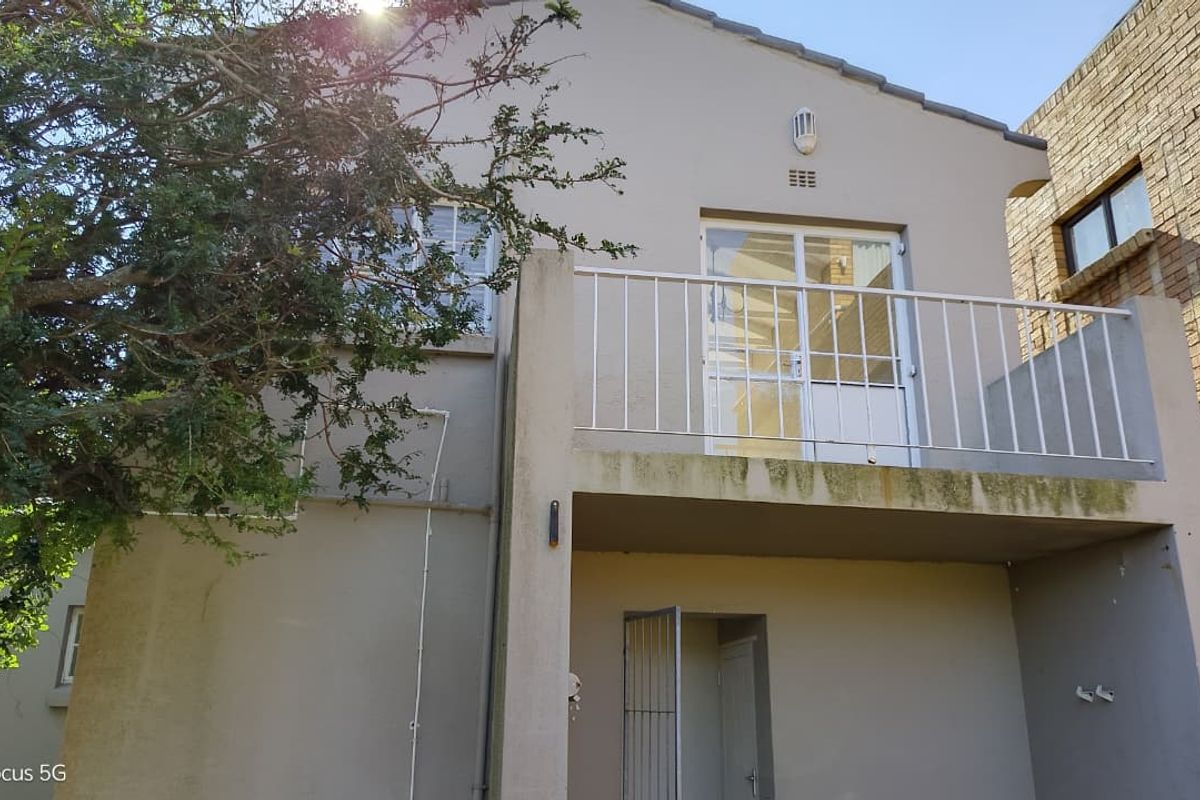 Rear exterior view of the property featuring a balcony with metal railings and visible signs of weathering on the building facade.