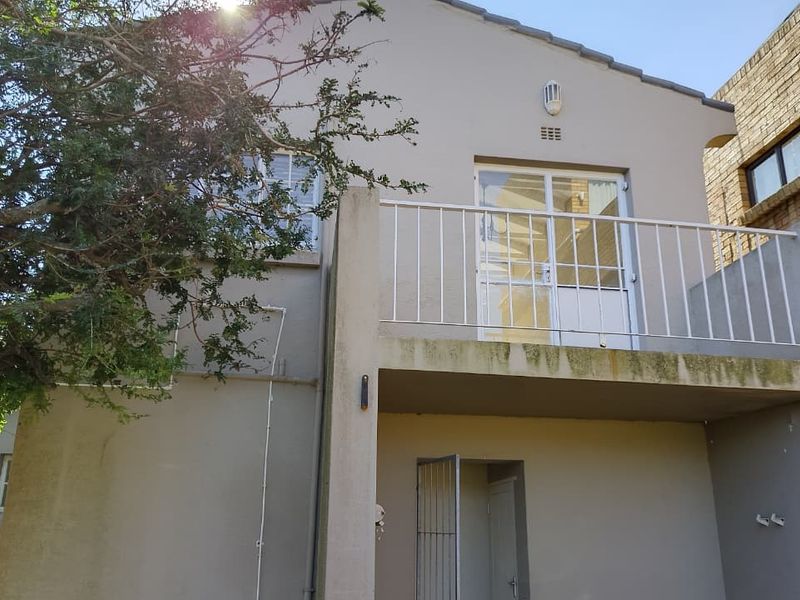 Rear exterior view of the property featuring a balcony with metal railings and visible signs of weathering on the building facade.