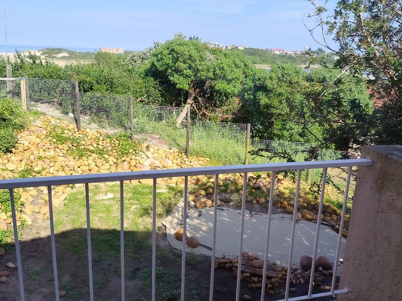 An elevated balcony area featuring a metal balustrade, overlooking a landscaped garden with rock features and coastal views.