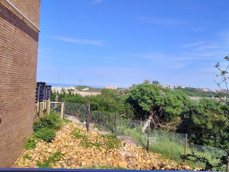 An elevated view overlooking coastal landscape and vegetation, featuring a brick exterior wall and wire mesh boundary fencing.