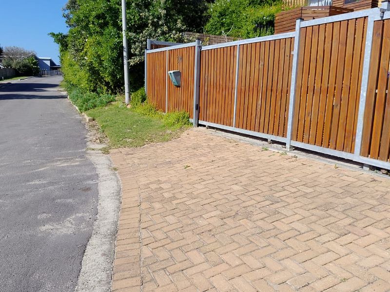 Street view showing the property entrance with a timber slat fence, metal sliding gate, and paved driveway area.