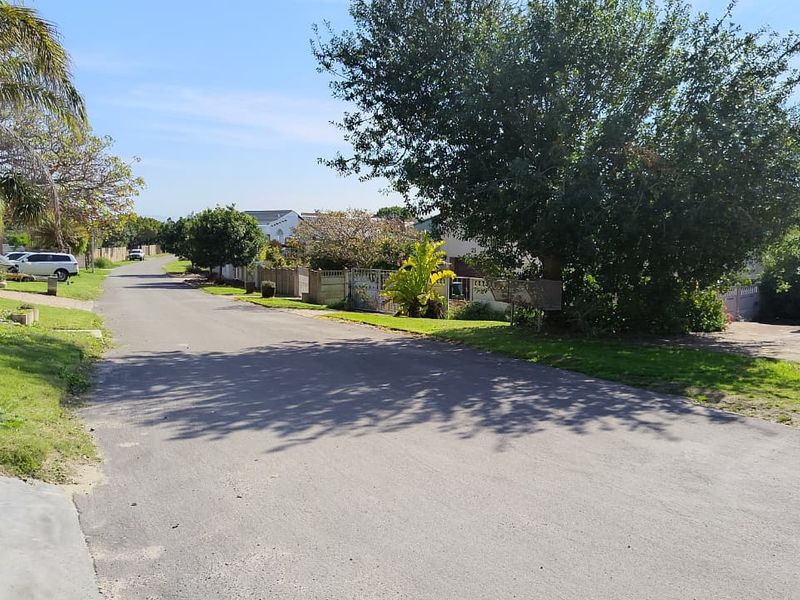 A view of the residential street approach showing the road, surrounding landscaping, and property boundary access.