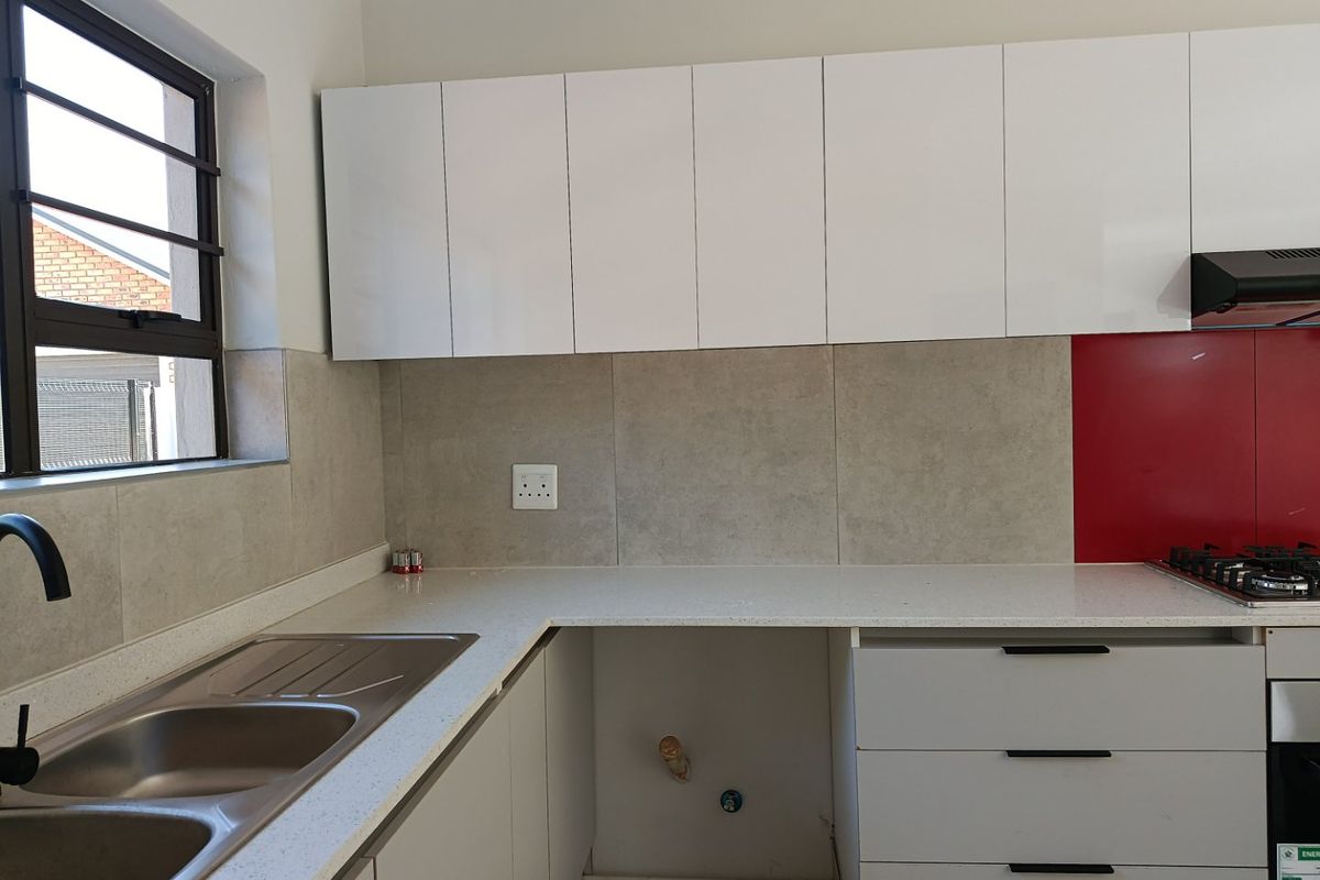 Modern kitchen featuring white cabinetry, stone countertops, a gas hob with extractor fan, and a tiled splashback with a dedicated appliance space.