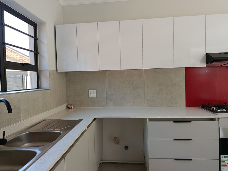 Modern kitchen featuring white cabinetry, stone countertops, a gas hob with extractor fan, and a tiled splashback with a dedicated appliance space.