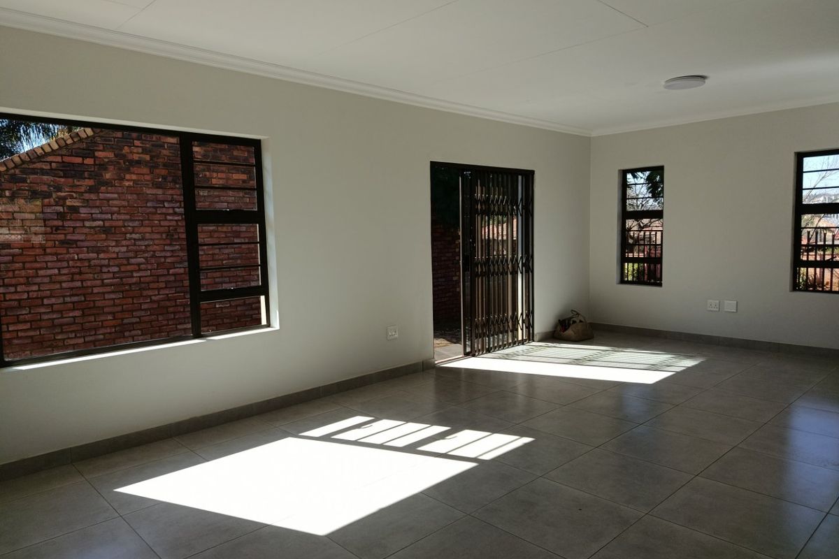A bright, spacious, and empty living area featuring neutral tiled flooring, clean white walls, and secure access to the exterior.