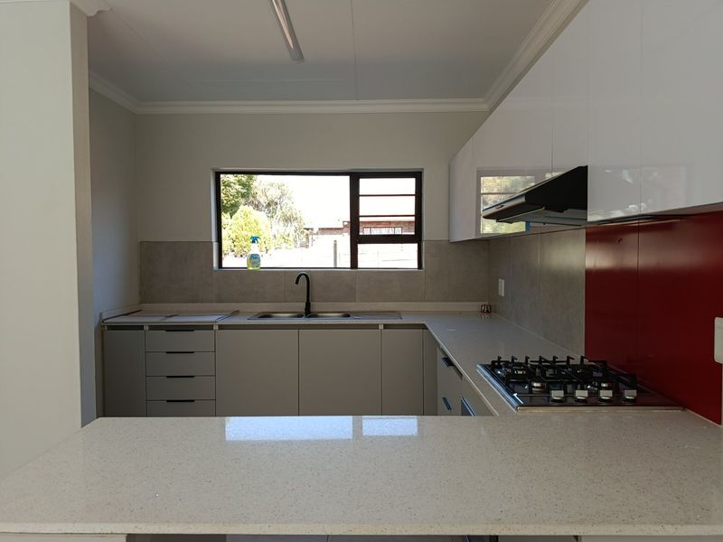 A modern, clean kitchen featuring quartz countertops, a gas hob with extractor fan, and ample cabinetry, offering a functional and well-maintained workspace.