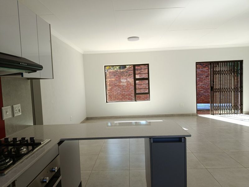Modern open-plan kitchen and living area featuring sleek cabinetry, stone countertops, built-in appliances, and tiled flooring with direct access to the exterior.