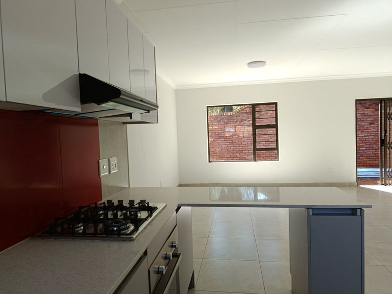 Modern kitchen featuring gloss cabinetry, stone countertops, a gas hob, and a breakfast bar, seamlessly flowing into an open-plan living area.