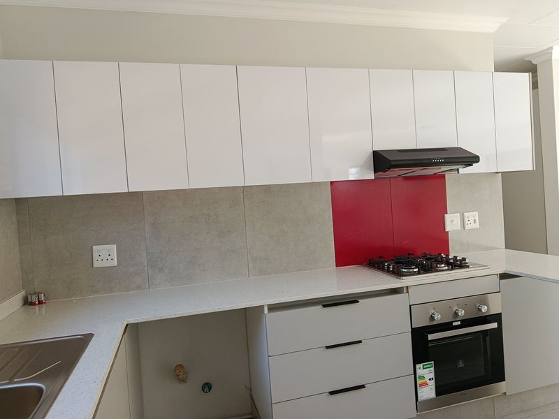 Modern kitchen featuring white gloss cabinetry, stone countertops, built-in oven, gas hob, and a striking red splashback panel.