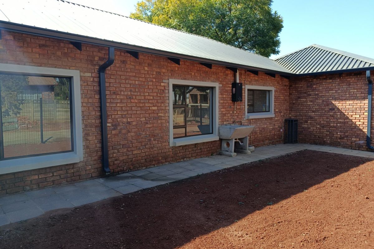 Rear exterior view of the house featuring face brick walls, metal roofing, aluminium window frames, and a concrete utility sink on a paved walkway.