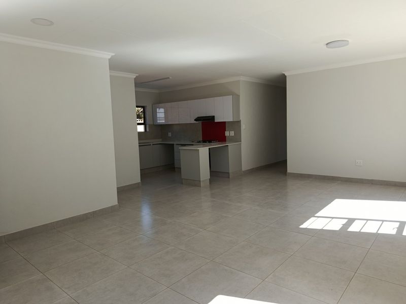 Spacious open-plan living area featuring a modern kitchen with built-in cabinetry, hob, and extractor fan, finished with neutral tiled flooring throughout.