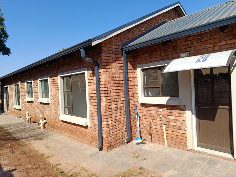 Rear exterior view of a face brick house featuring aluminium window frames, metal roofing, and a paved walkway along the building perimeter.