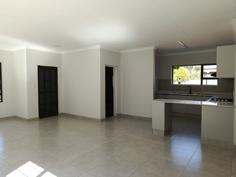 Spacious open-plan living area featuring neutral tiled flooring, coved cornicing, and a modern kitchen with a breakfast island and built-in gas hob.
