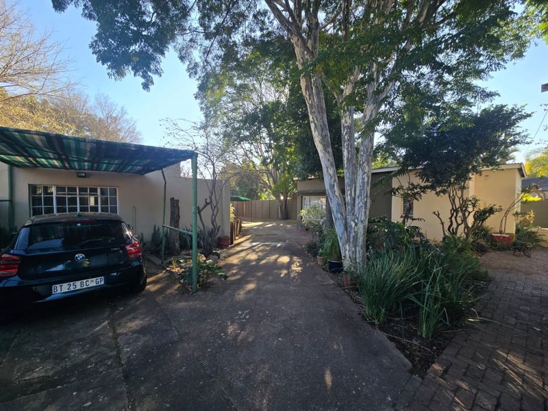 Front exterior view of the property featuring a concrete driveway, a covered carport, and established garden landscaping with mature trees.