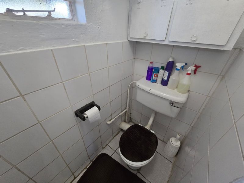 A compact, dated bathroom featuring a standard toilet, wall-mounted storage cabinets, and white ceramic wall tiling.
