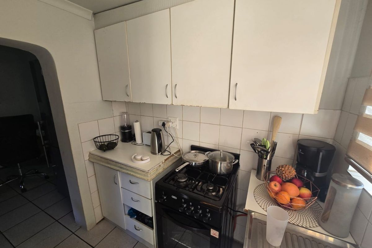 A compact kitchen featuring white cabinetry, a tiled backsplash, a gas stove with oven, and a stainless steel sink.