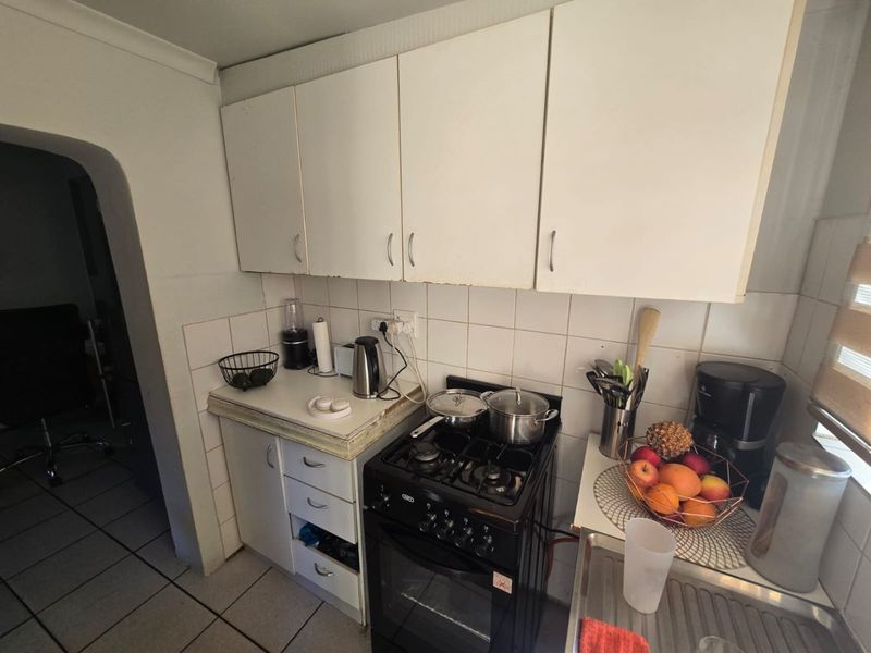 A compact kitchen featuring white cabinetry, a tiled backsplash, a gas stove with oven, and a stainless steel sink.