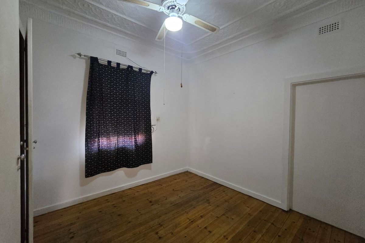 An empty bedroom featuring original timber flooring, a decorative pressed metal ceiling, and a central ceiling fan.